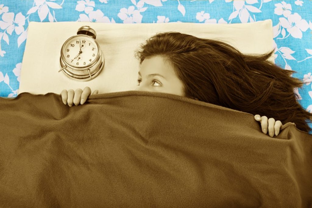 Young girl in bed hiding beneath her blanket from the alarm clock noise